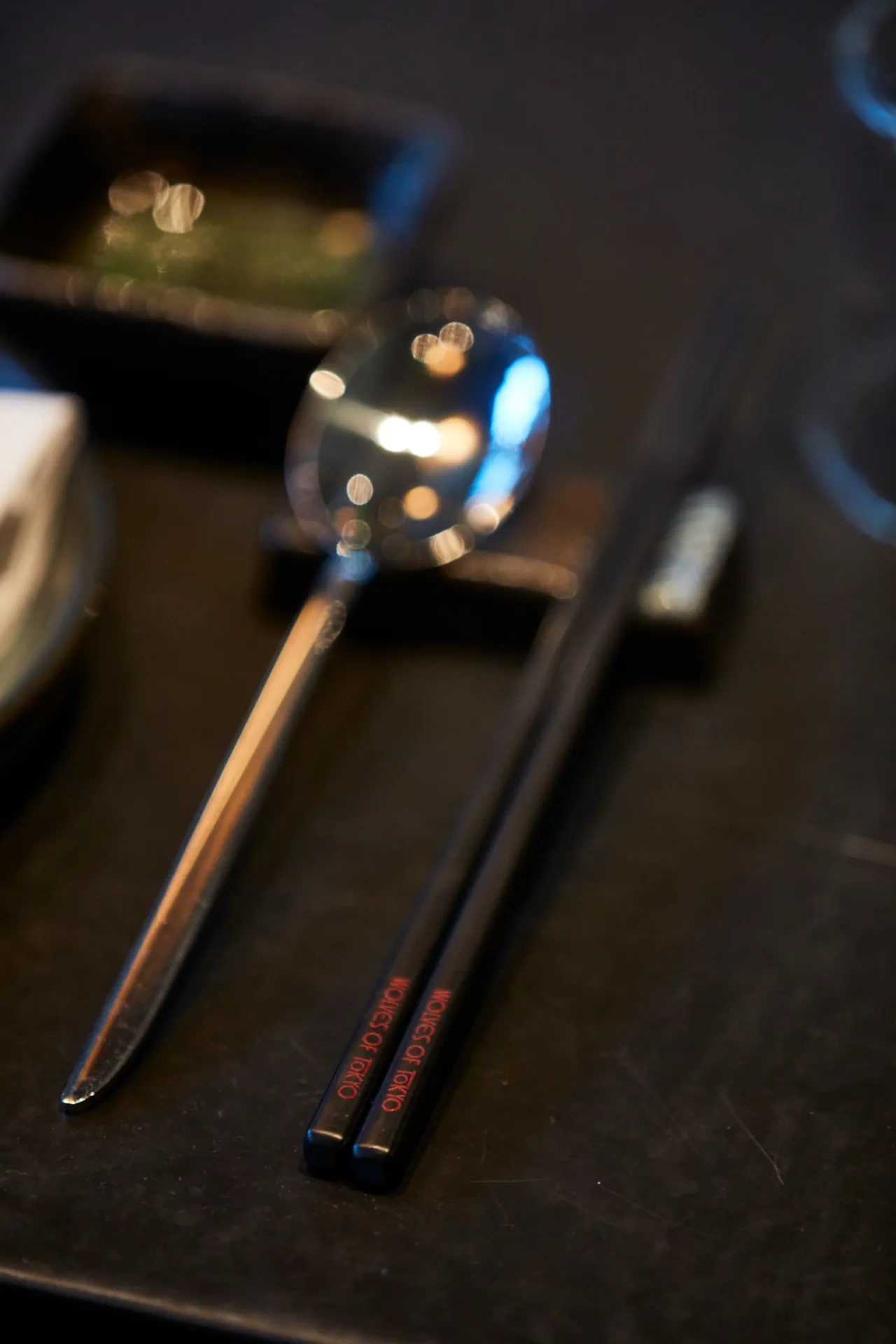 Blurred close-up of chopsticks and a decorative holder with warm and cool lighting against a dark surface at Wolves of Tokyo restaurant