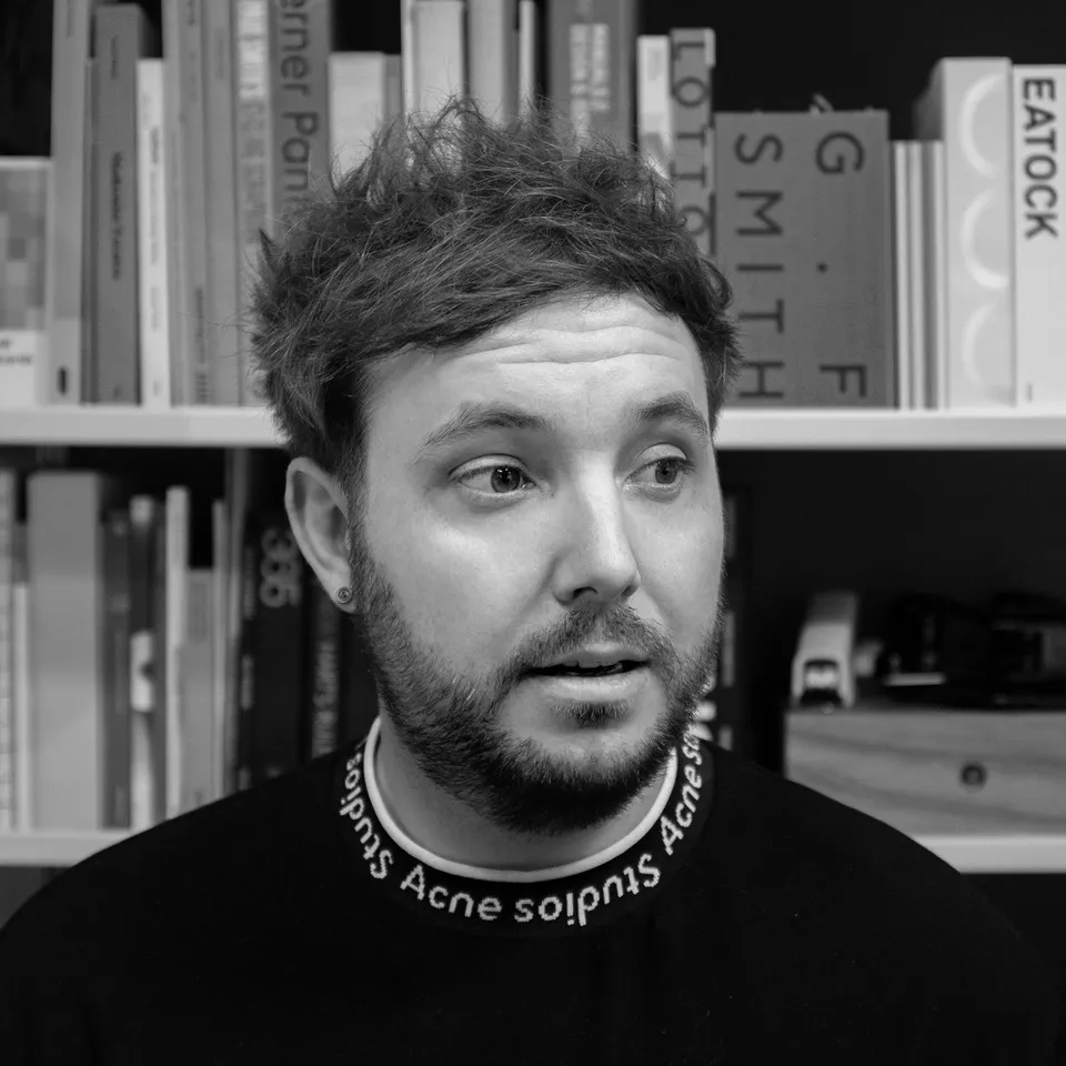 Mark Jones, creative director at Studio Blackburn, pictured against a bookshelf in black and white