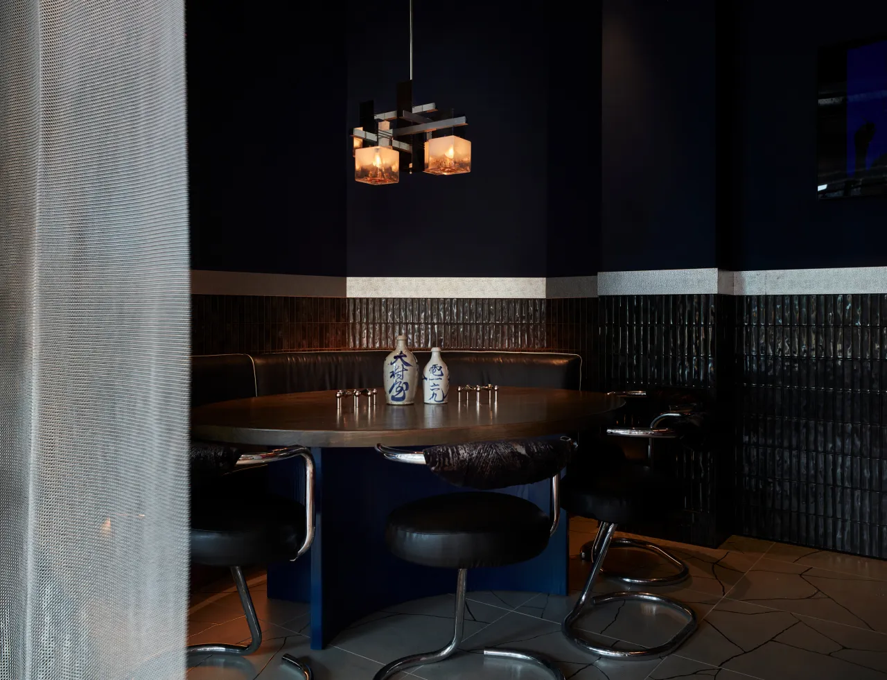 Dimly lit dining area at Wolves of Tokyo with a wooden table set with blue chairs, pendant lights overhead, and dark wood panelling on the walls