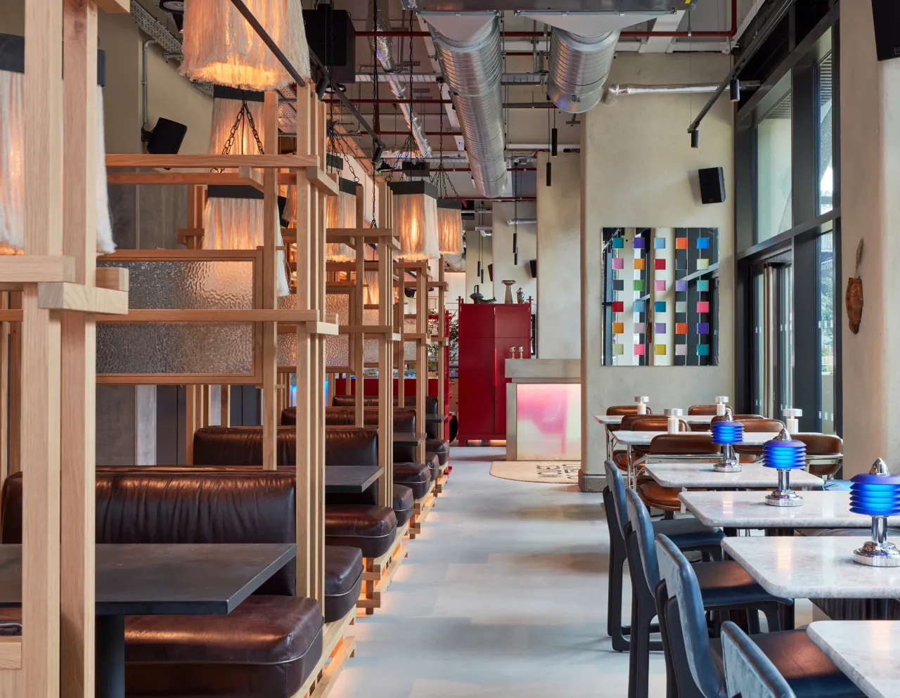 Interior of Wolves of Tokyo restaurant showing wooden booth seating on the left, dining tables with blue glassware on the right, and colourful artwork on the walls